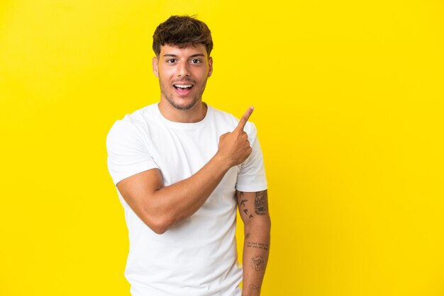 Young caucasian handsome man isolated on yellow background surprised and pointing side