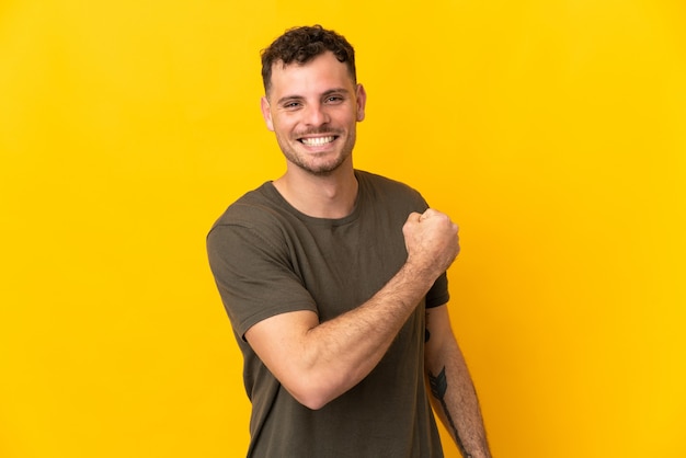 Young caucasian handsome man isolated on yellow wall celebrating a victory