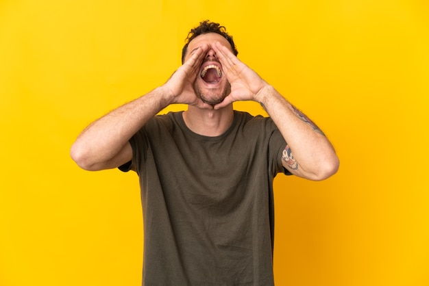 Foto giovane uomo caucasico bello isolato sulla parete gialla che grida e che annuncia qualcosa