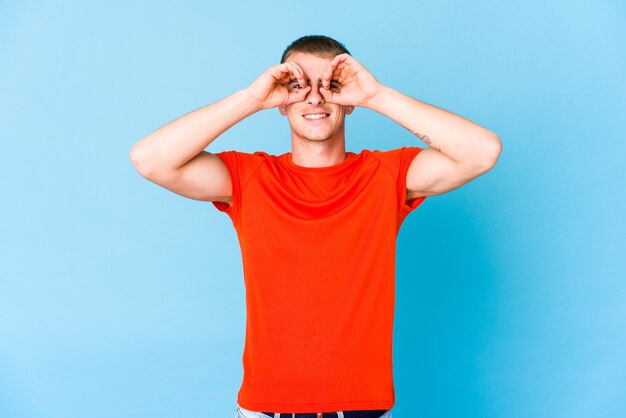 Young caucasian handsome man showing okay sign over eyes