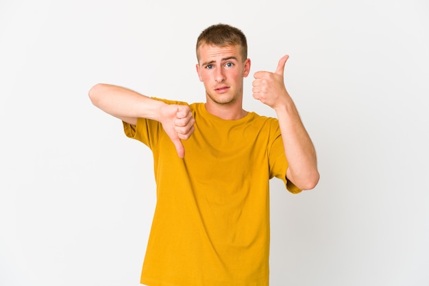 Young caucasian handsome man showing thumbs up and thumbs down, difficult choose concept