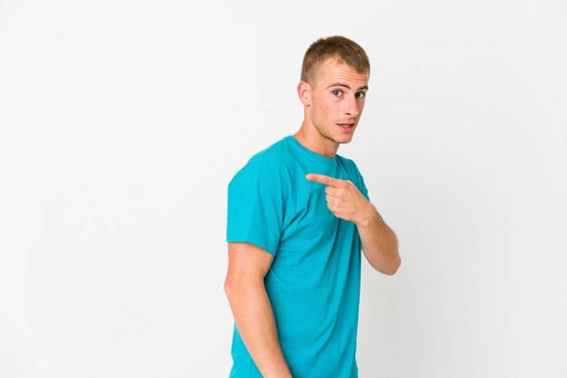 Young caucasian handsome man smiling and pointing aside, showing something at blank space.