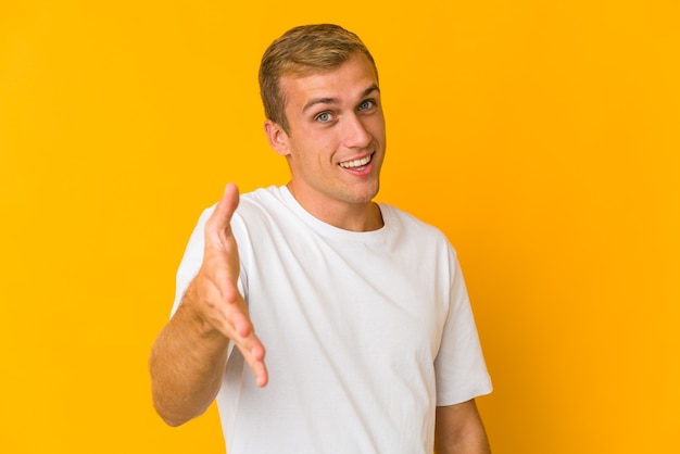 Giovane uomo caucasico bello che allunga la mano alla macchina fotografica nel gesto di saluto.