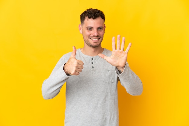 Young caucasian handsome man on yellow counting six with fingers