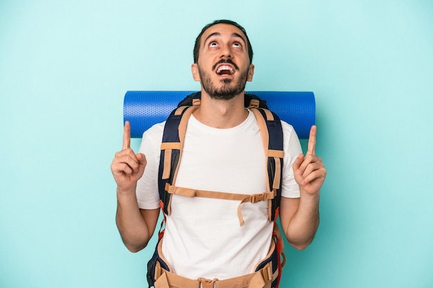 口を開けて逆さまを指している青い背景に分離された若い白人ハイカー男。