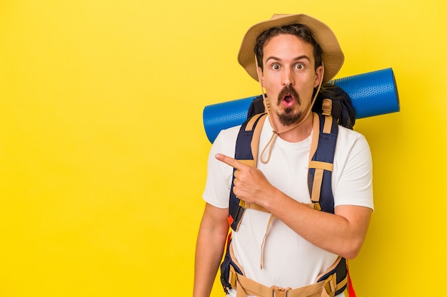 Young caucasian hiker man isolated on yellow background pointing to the side