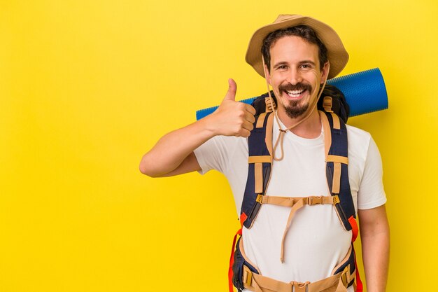 Young caucasian hiker man isolated on yellow background smiling and raising thumb up