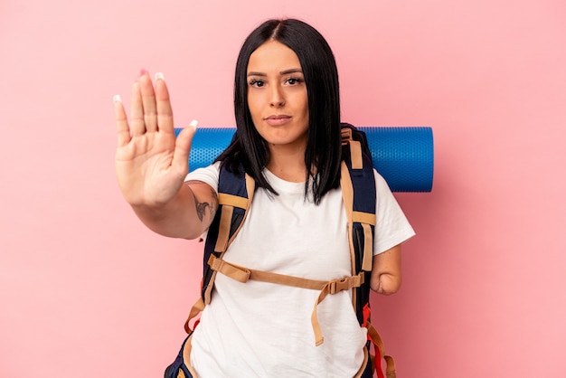 Young caucasian hiker woman with one arm isolated on pink background standing with outstretched hand showing stop sign, preventing you.