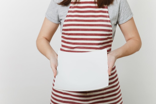 Young caucasian housewife in striped apron, gray t-shirt isolated. Housekeeper woman holding in hands white empty square plate