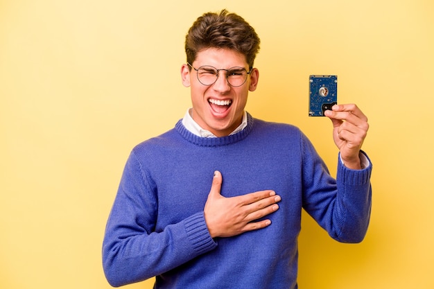 Young caucasian informatics man isolated on yellow background laughs out loudly keeping hand on chest