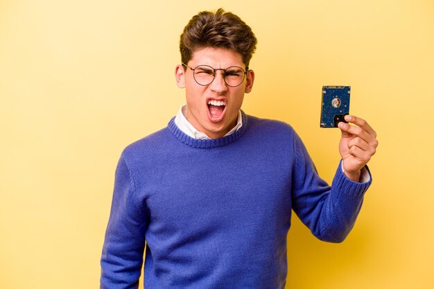 Young caucasian informatics man isolated on yellow background screaming very angry and aggressive