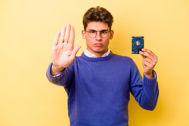 Молодой кавказский информатик, изолированный на желтом фоне, стоит с протянутой рукой, показывая знак "стоп", мешающий вам