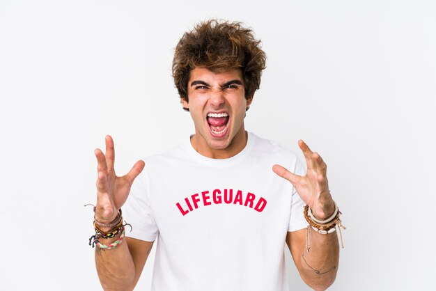 Young caucasian life guard against a white wall isolated screaming with rage.