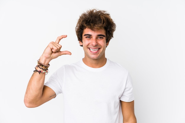 Young caucasian life guard on white background isolated holding something little with forefingers, smiling and confident.