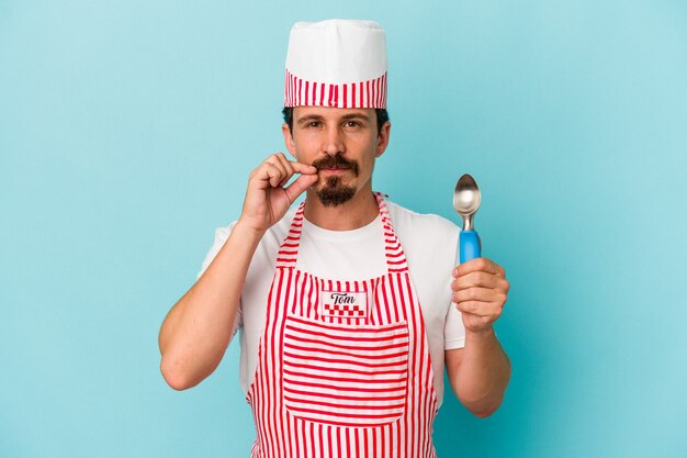 Young caucasian maker holding a scoop isolated on blue background with fingers on lips keeping a secret.