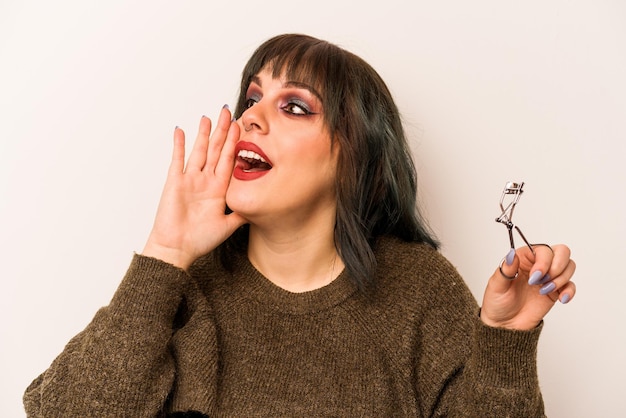 Young caucasian makeup artist woman holding a eyelash curler isolated on white background shouting and holding palm near opened mouth