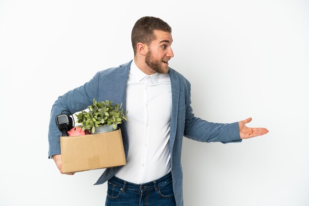 Young caucasian making a move while picking up a box full of things isolated on white background with surprise expression while looking side