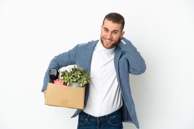 Young caucasian making a move while picking up a box full of things isolated on white wall laughing