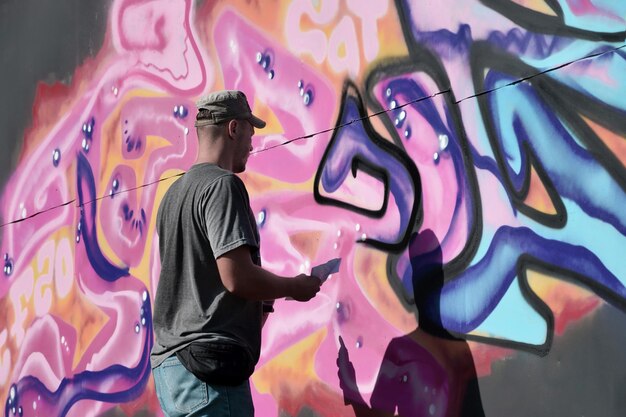 Young caucasian male graffiti artist drawing big street art painting in blue and pink tones