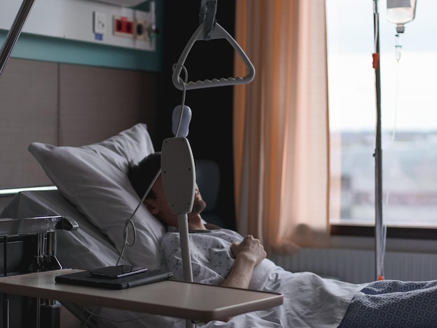 A young caucasian male patient lies in bed with a dropper in his hand and sleeps after surgery