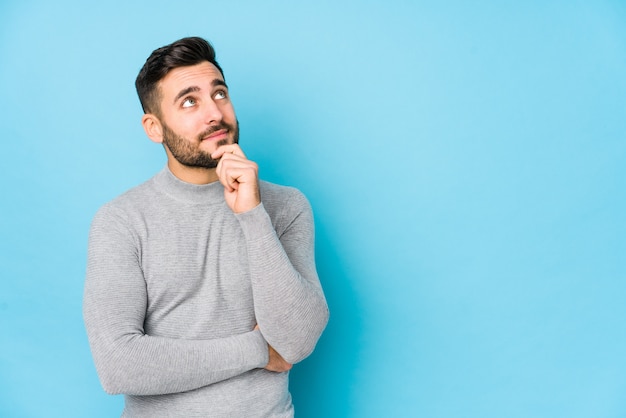 Photo young caucasian man against a blue isolated looking sideways with doubtful and skeptical expression.