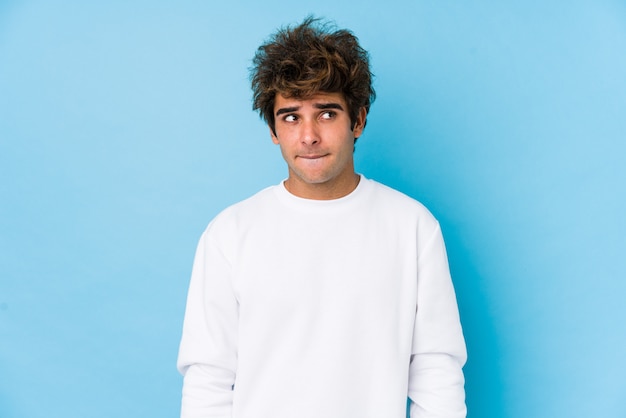 young caucasian man against a blue wall isolated confused, feels doubtful and unsure.