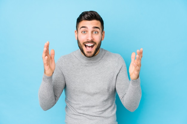 Young caucasian man against a blue wall isolated receiving a pleasant surprise, excited and raising hands.