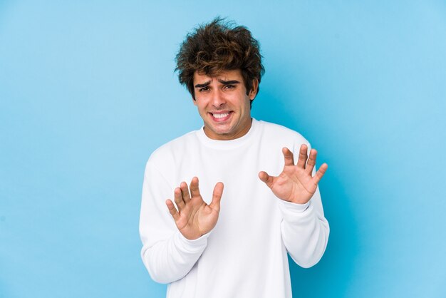 Young caucasian man against a blue wall isolated rejecting someone showing a gesture of disgust.
