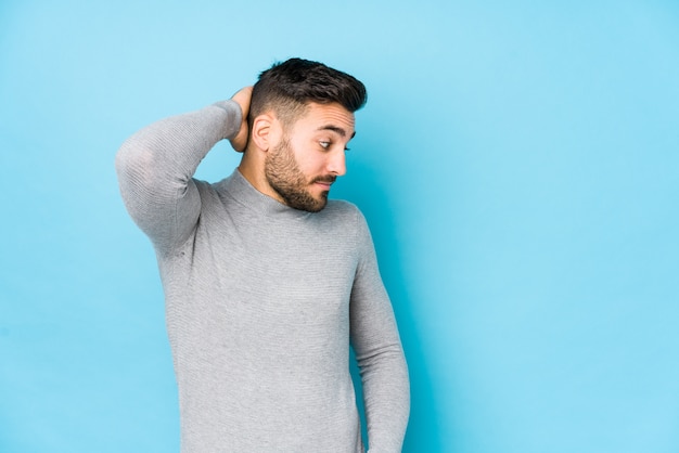 Young caucasian man against a blue wall isolated touching back of head, thinking and making a choice.