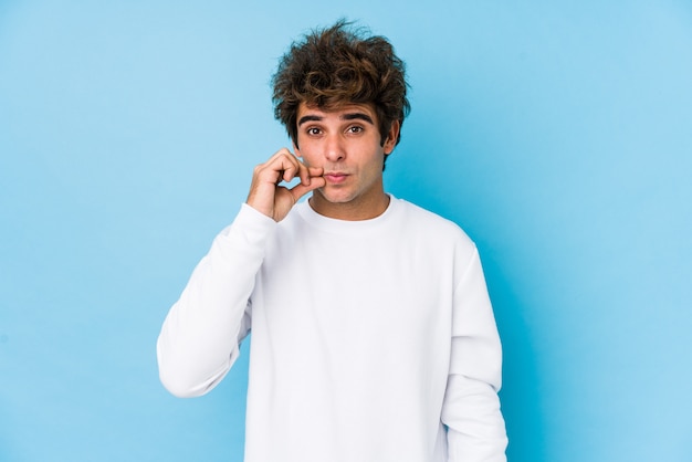 Young caucasian man against a blue wall isolated with fingers on lips keeping a secret.