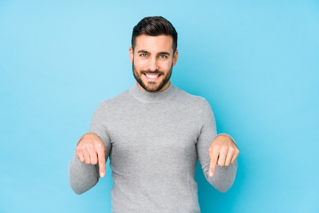 Young caucasian man against a blue wall points down with fingers