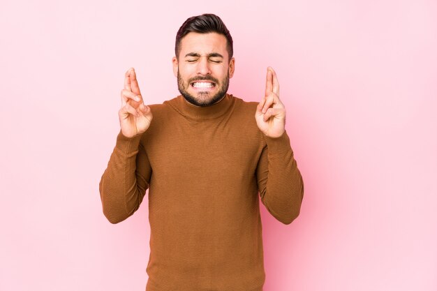 Young caucasian man against a pink background isolated crossing fingers for having luck