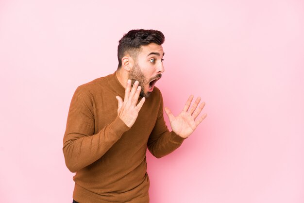 Young caucasian man against a pink background isolated shouts loud, keeps eyes opened and hands tense.