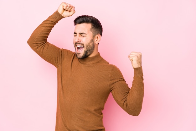 Il giovane uomo caucasico contro una rosa isolata che celebra un giorno speciale, salta e alza le braccia con energia.