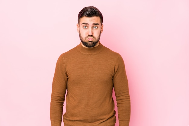 Young caucasian man against a pink wall isolated blows cheeks, has tired expression. Facial expression concept.