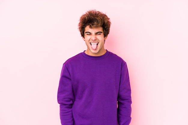 Young caucasian man against a pink wall isolated funny and friendly sticking out tongue.