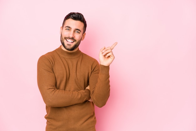 Young caucasian man against a pink wall isolated smiling cheerfully pointing with forefinger away.