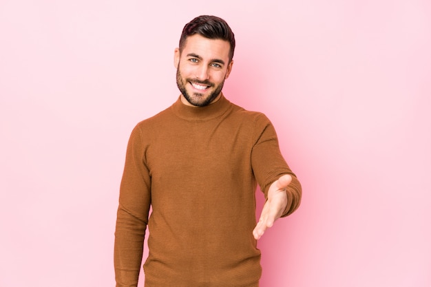 Young caucasian man against a pink wall isolated stretching hand