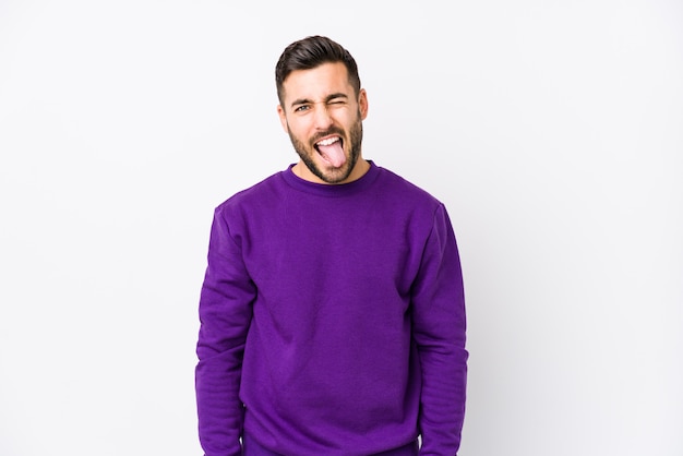 Young caucasian man against a white wall funny and friendly sticking out tongue.