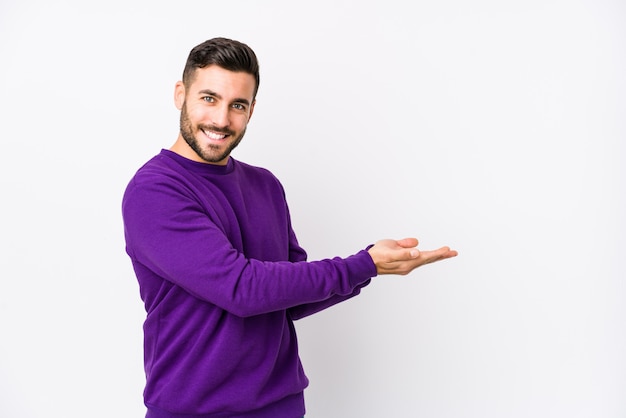 Young caucasian man against a white wall holding a blank space on a palm.