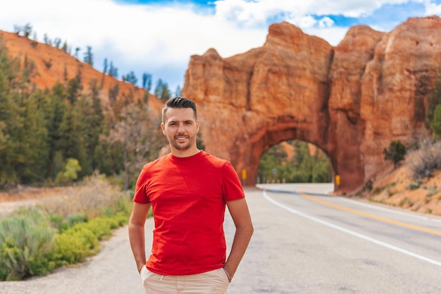 Young caucasian man in background of natural stone arch Bridge in the Red Canyon National Park in Utah USA