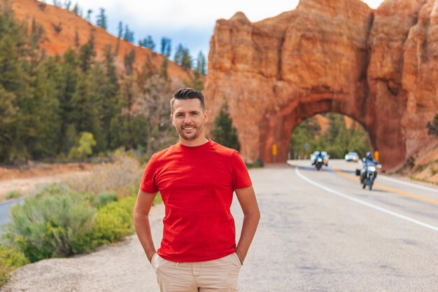 Young caucasian man in background of natural stone arch Bridge in the Red Canyon National Park in Utah USA