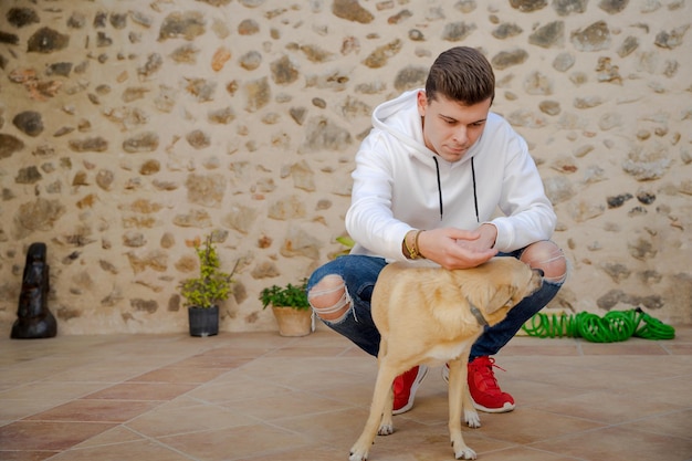 Young Caucasian man in the backyard with a dog In the background is a wall of stones