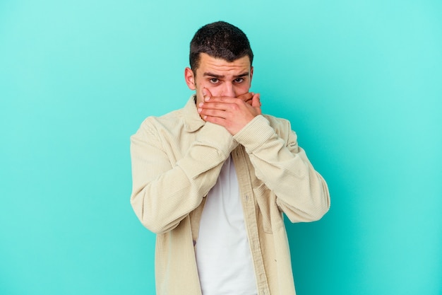 Young caucasian man on blue covering mouth with hands looking worried.