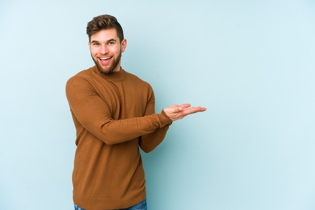 Young caucasian man on blue holding a copy space on a palm.