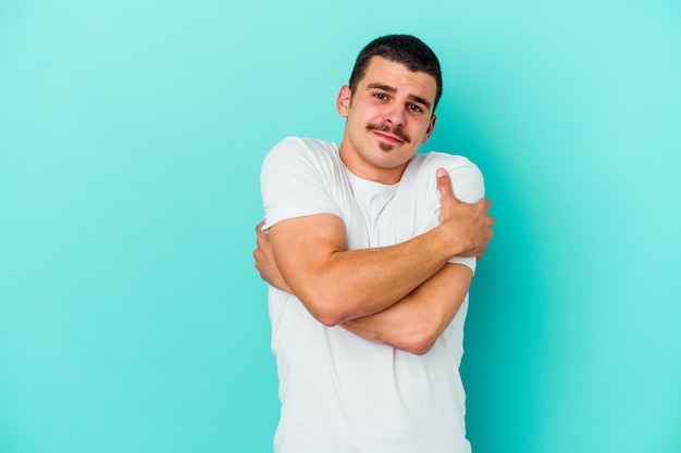 Young caucasian man on blue hugs, smiling carefree and happy.