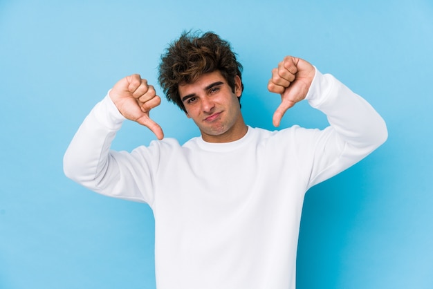 Young caucasian man on blue isolated showing thumb down and expressing dislike.