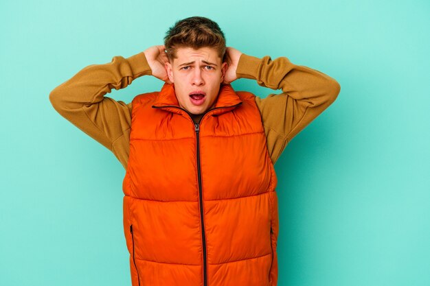 Young caucasian man on blue screaming with rage.