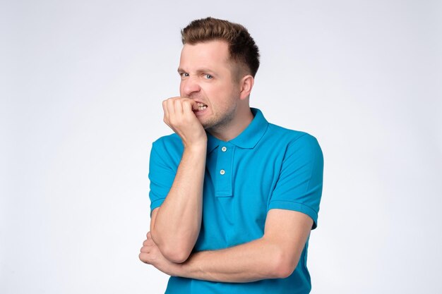 Young caucasian man in blue shirt biting nails being stressed or nervous