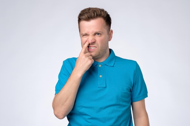 Young caucasian man in blue shirt picking in his nose